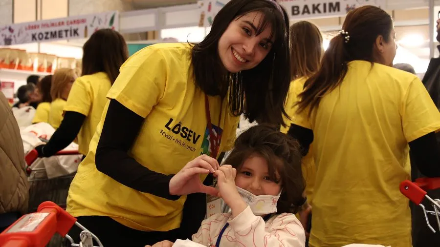 LÖSEV çalışanı yardım dağıtımında, lösemili çocukla sevgi dolu an. Elleriyle kalp işareti yapıyorlar. 