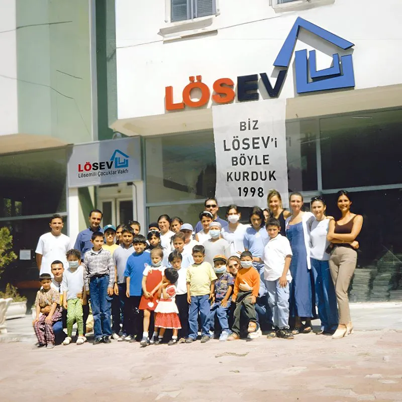 LÖSEV’in 1998 yılındaki kuruluş gününden bir fotoğraf. Kurucu Başkan Dr. Üstün Ezer ve kurucu ekip, Ankara’daki ilk vakıf binasında “Bir masa, bir sandalyeden doğan umut” sloganıyla LÖSEV’in temellerini atıyor.